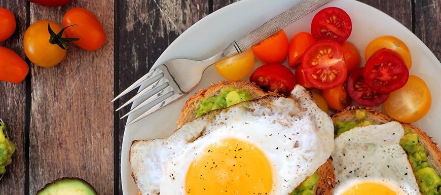 Healthy avocado, egg open sandwiches on a plate with cherry tomatoes on rustic wood